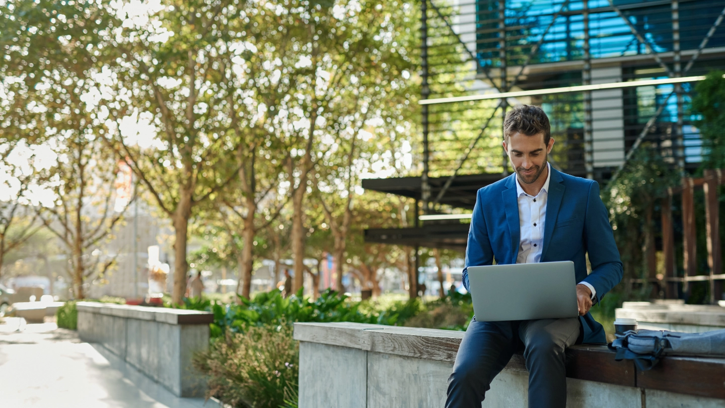 young businessman working online with laptop sitting outside